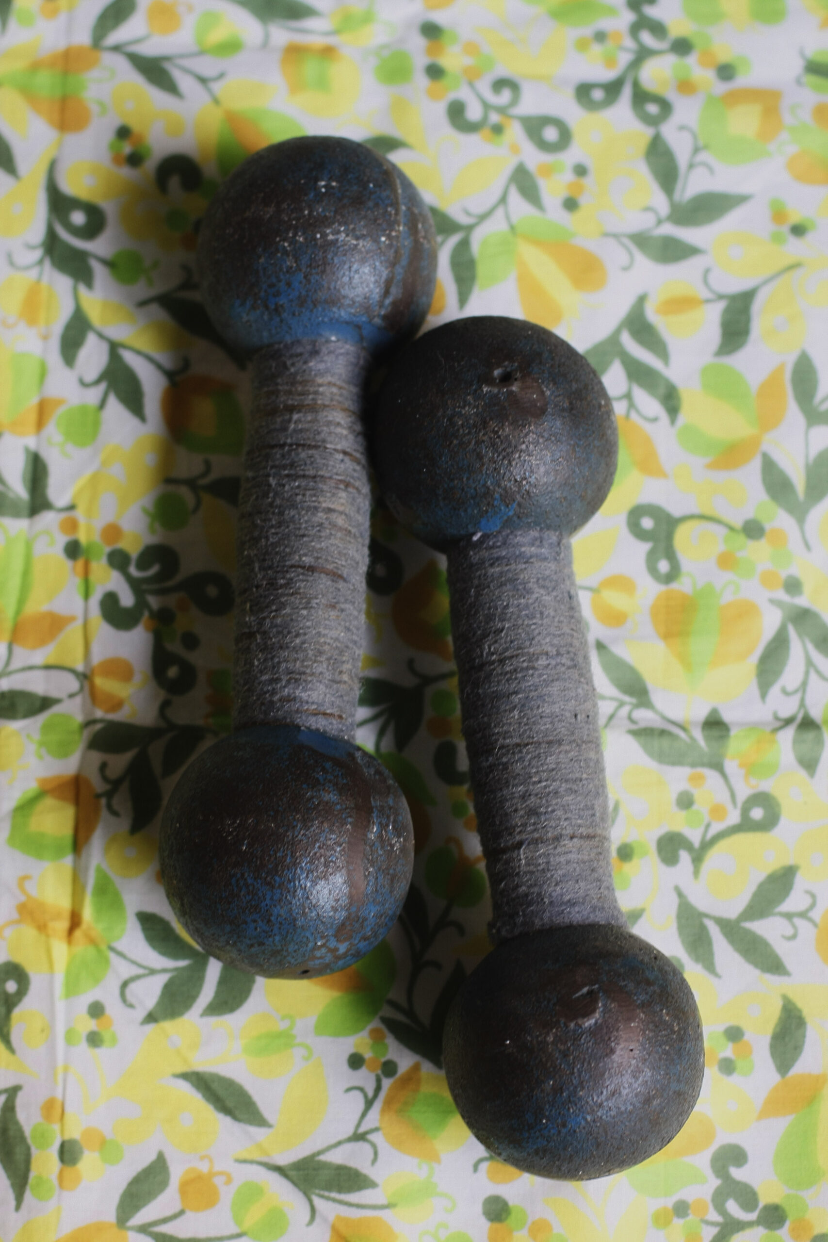 Two dark metal dumbbells with wrapped handles resting on green-and-yellow patterned fabric.