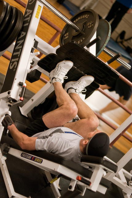 Exerciser reclining on a plate-loaded leg press with both feet on the platform and knees bent.
