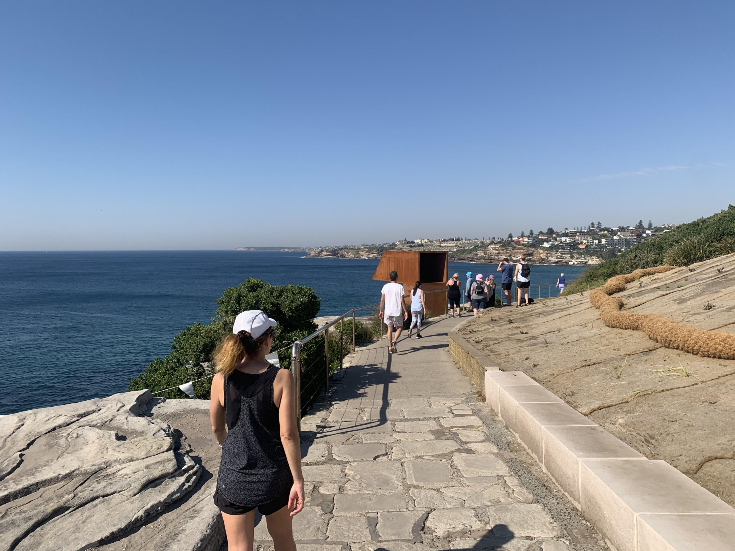 People walking along a paved coastal path beside the ocean.